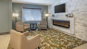 Un salon avec des fauteuils beiges, une cheminée, un téléviseur à écran plat et un tapis à motifs.