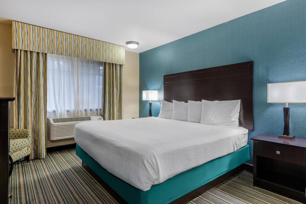 Ein Hotelzimmer mit einem großen Bett, zwei Nachttischen mit Lampen, einem Fenster mit Vorhängen und einer Klimaanlage.
