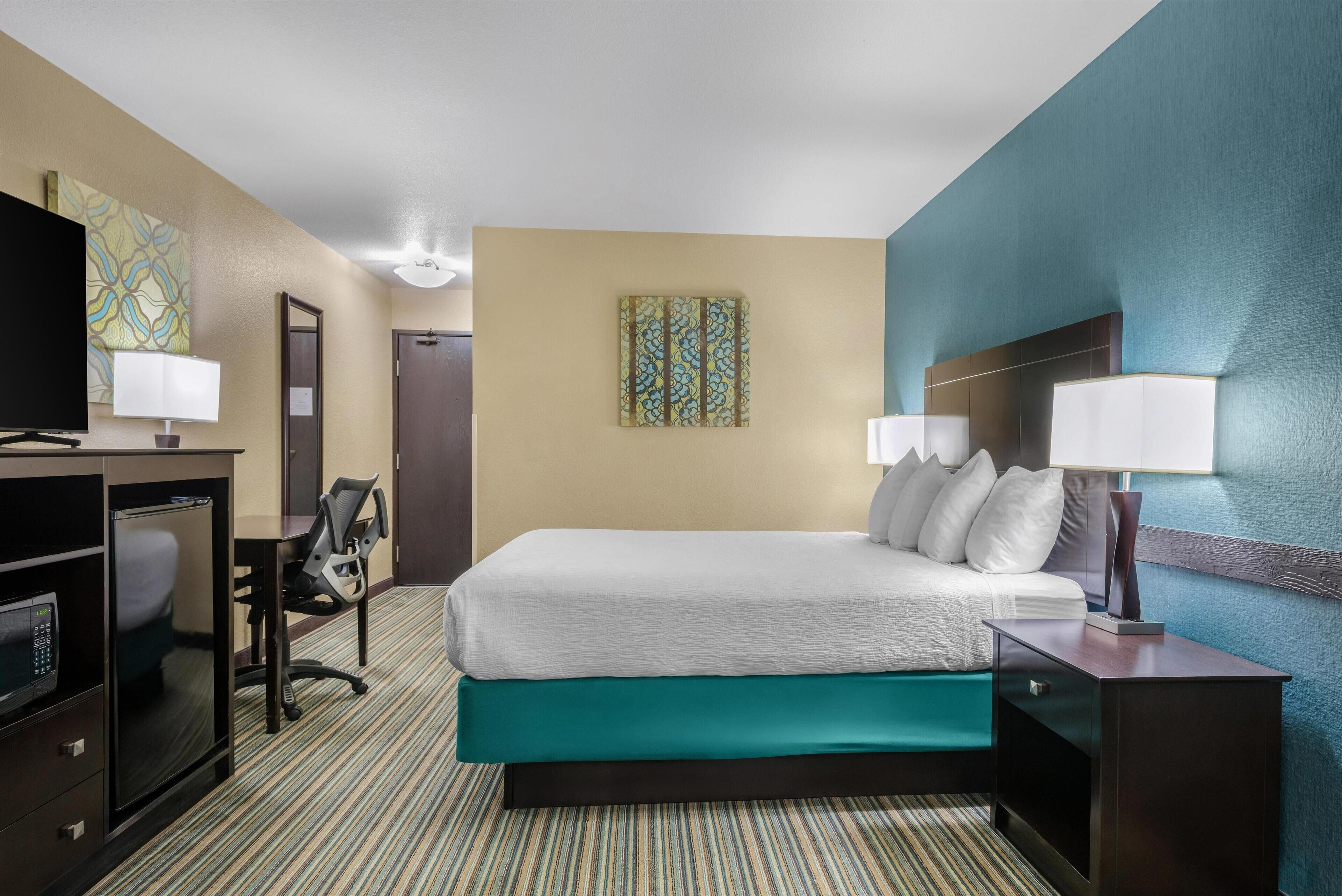 Una camera d'albergo con un letto, una scrivania, una sedia, una televisione e opere d'arte alle pareti.