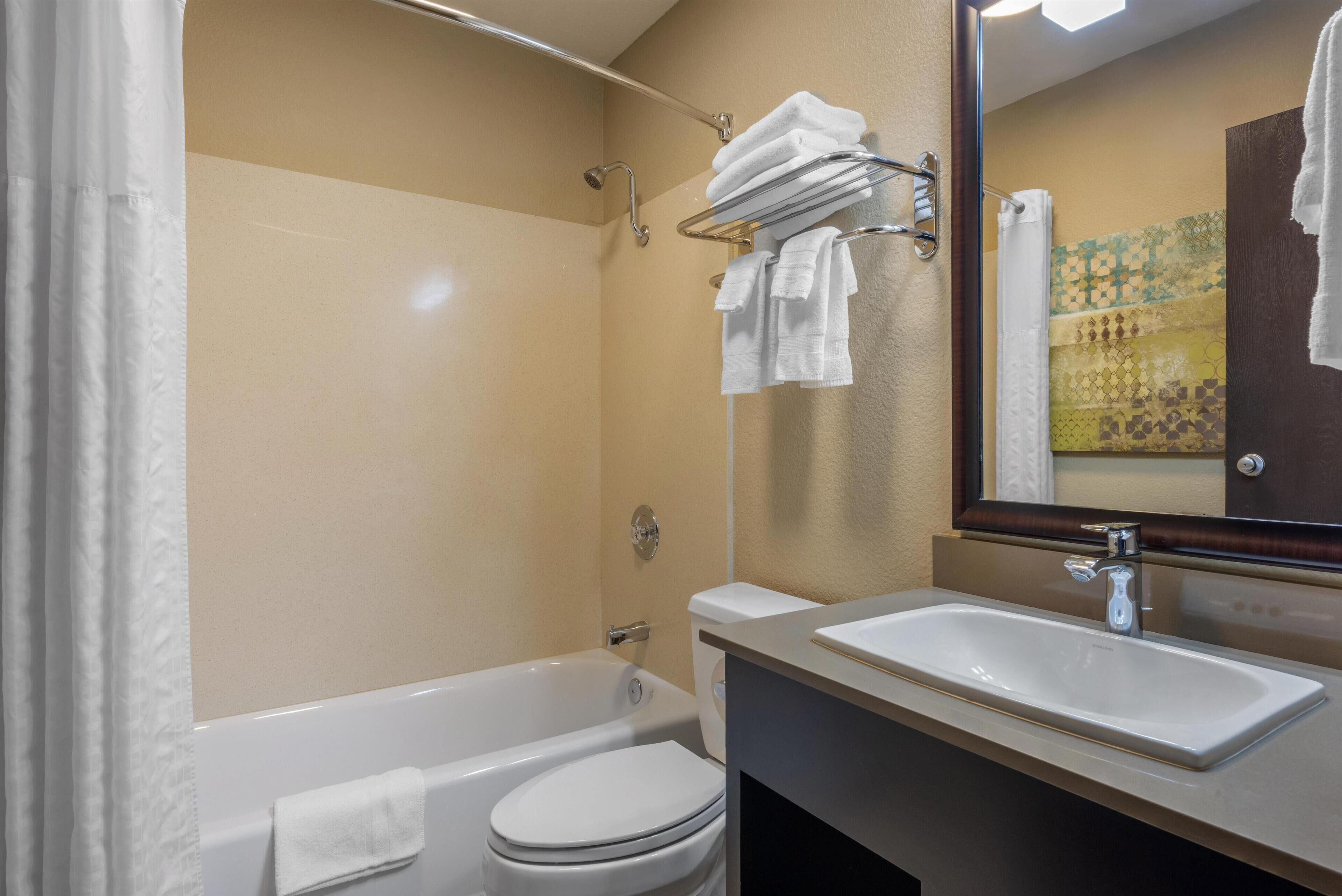 Un baño con bañera, inodoro, lavamanos y un perchero con toallas.