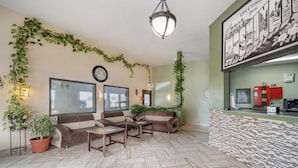 A reception area with a sofa, coffee table, and potted plants. There is a clock on the wall and a framed picture above the reception desk.