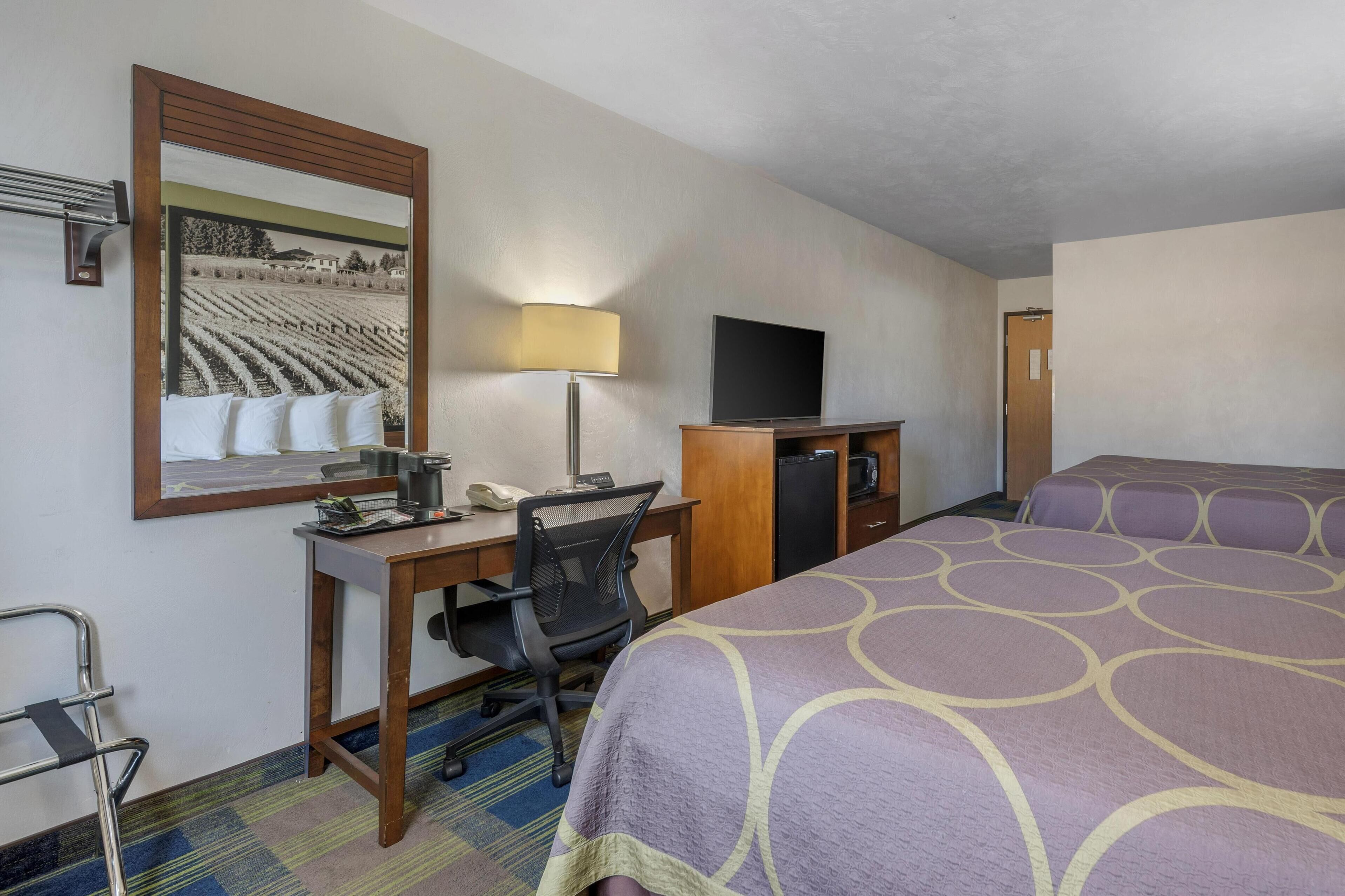 A hotel room with a bed, desk, chair, TV, and a mirror.
