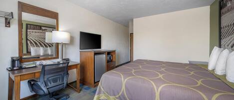 Habitación de hotel con cama, escritorio, silla, televisor y refrigerador pequeño.