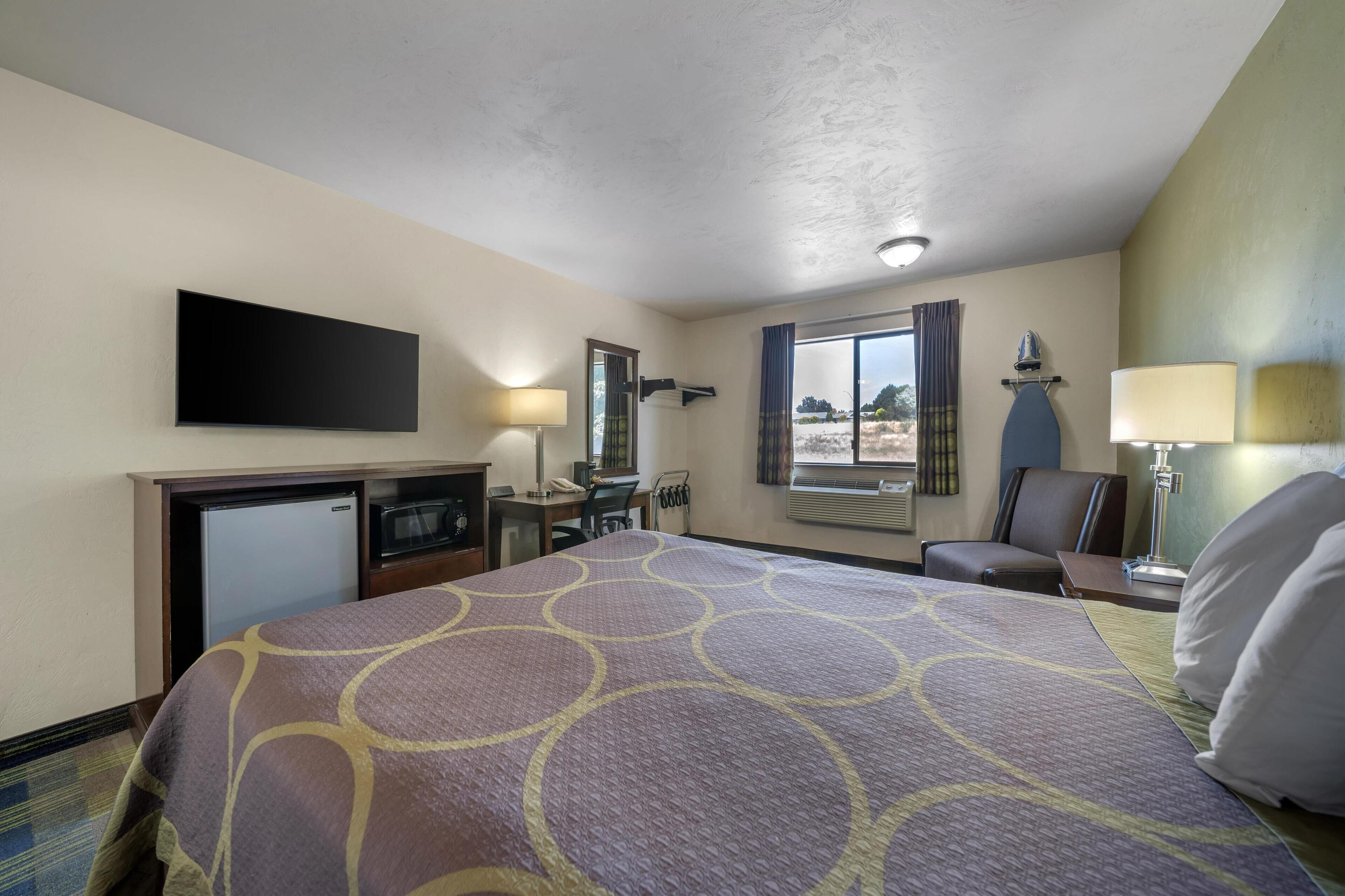 A hotel room with a bed, desk, chair, TV, and window with curtains.