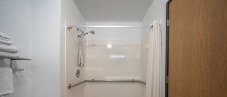 Eine ebenerdige Dusche mit Glastür, ein weißes Waschbecken und ein Handtuchhalter.