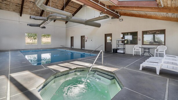 A swimming pool with a hot tub, lounge chairs, and a table with chairs.