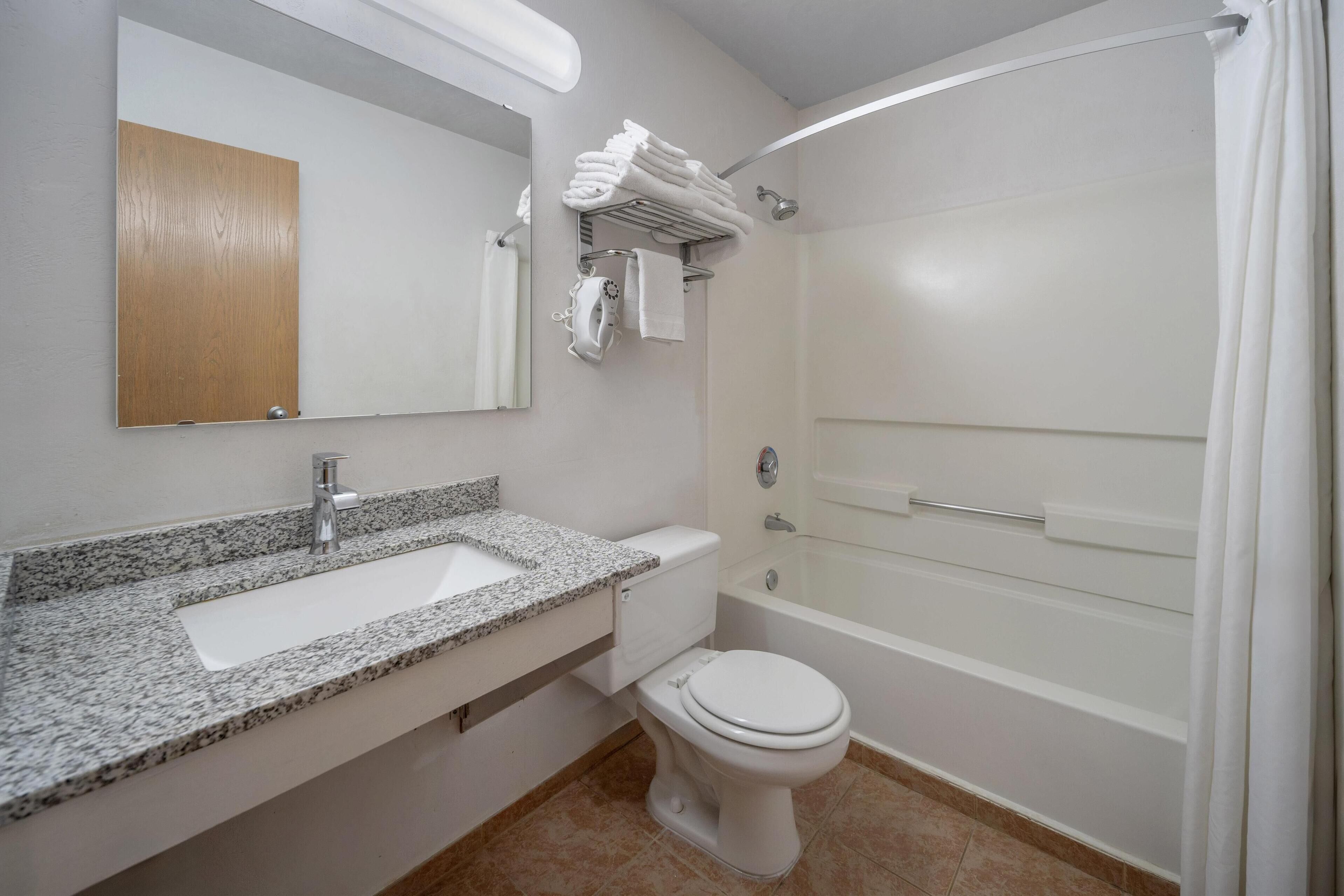 Un baño con lavamanos de granito, inodoro, bañera y toallero con toallas dobladas.
