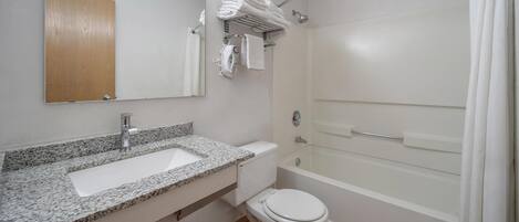Un baño con lavamanos de granito, inodoro, bañera y toallero con toallas dobladas.