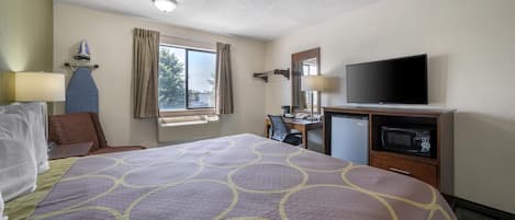 Habitación de hotel con una cama grande, un escritorio con computadora, televisor y microondas.