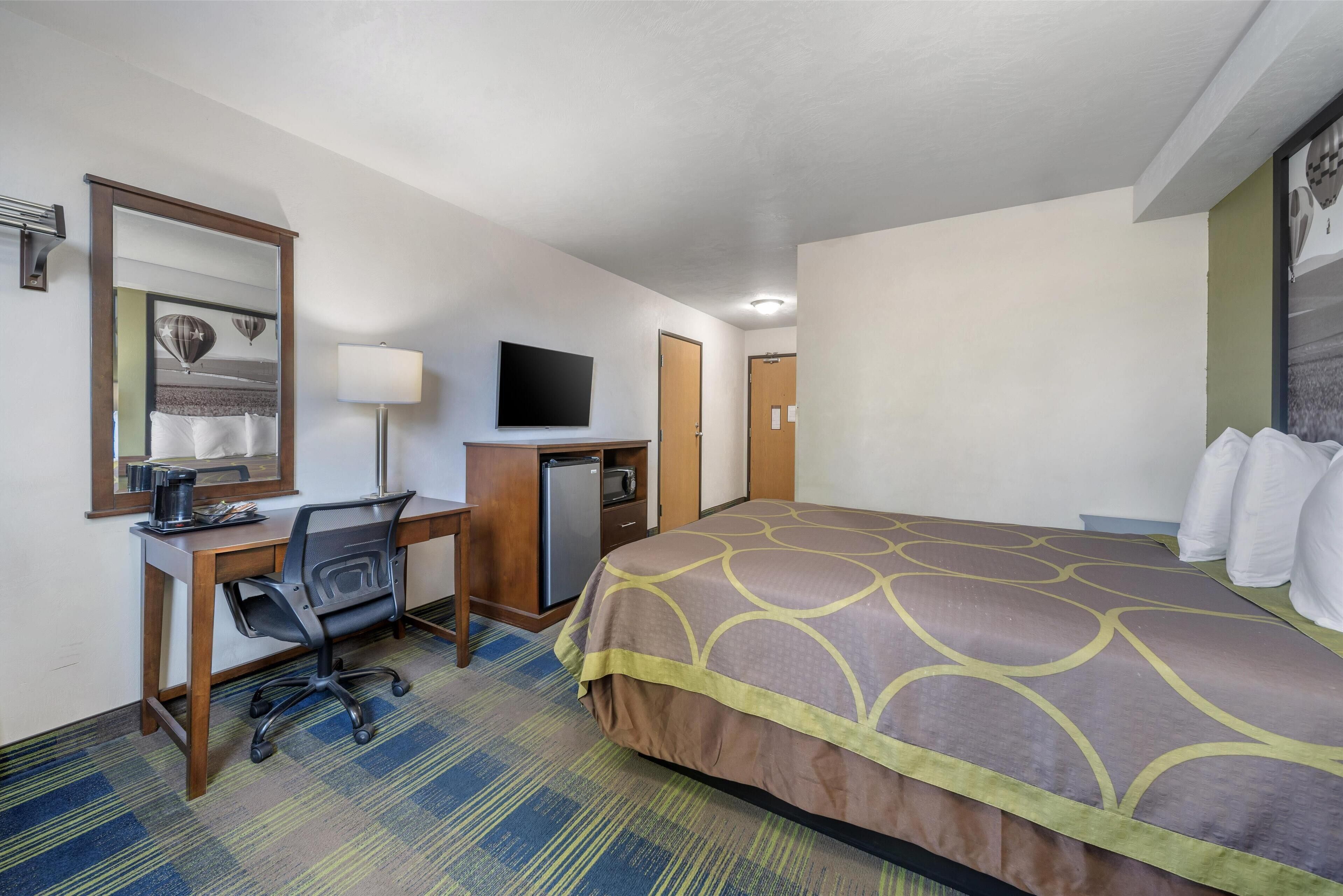 Habitación de hotel con cama, escritorio, silla, televisor y refrigerador pequeño.
