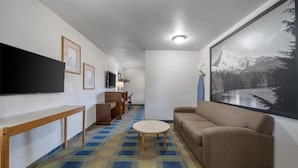 A hotel room with a sofa, a TV mounted on the wall, a large framed picture, and a patterned carpet.