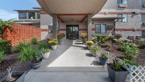 A building entrance with a covered walkway, potted plants, and a white picket fence.