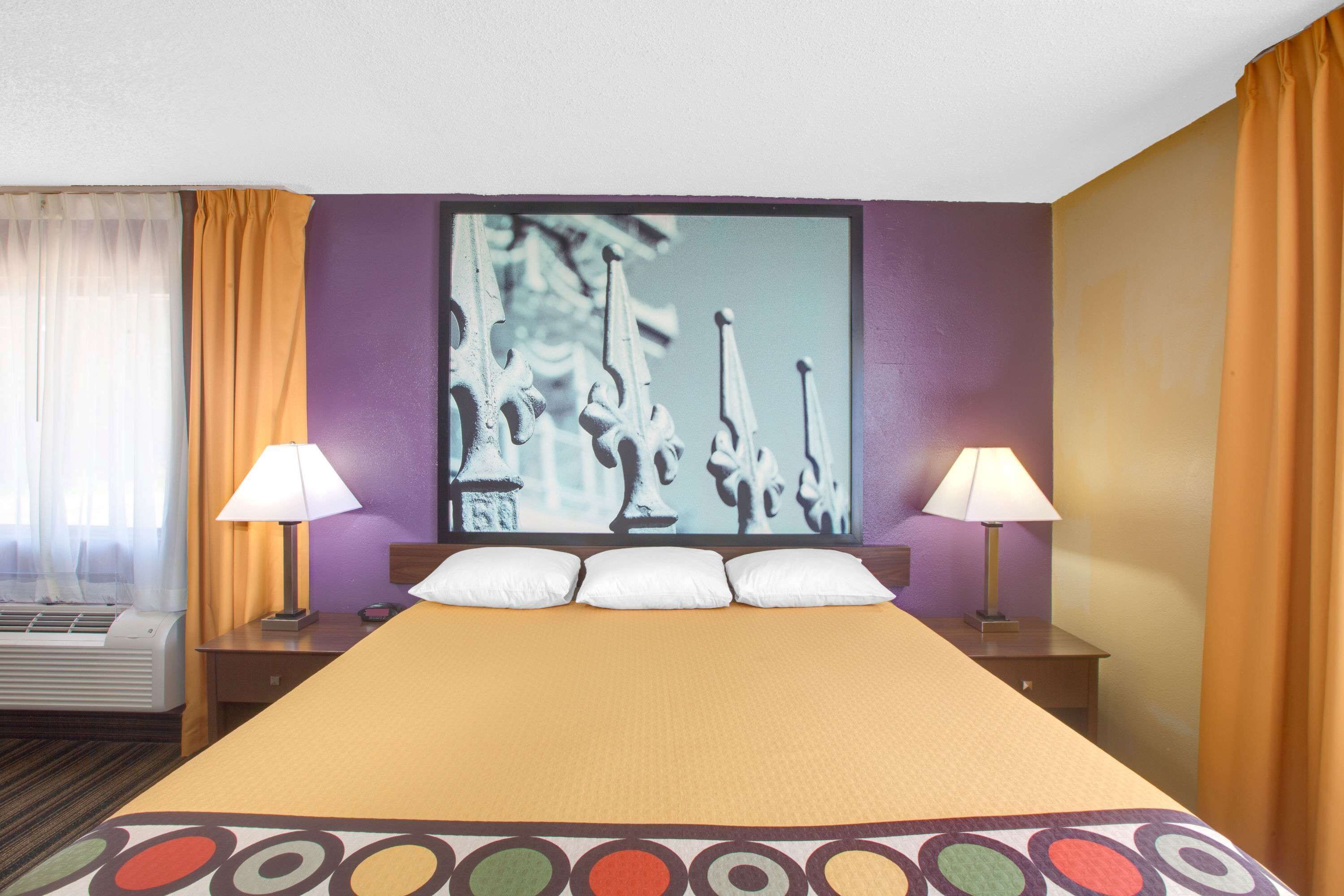 Habitación de hotel con una cama grande, dos mesitas de noche con lámparas, aire acondicionado de pared y una ventana con cortinas.