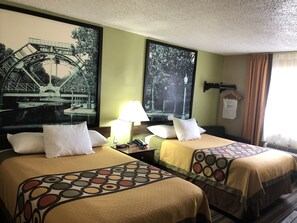 A hotel room with two beds, each with a patterned bedspread, a nightstand with a lamp, and a large framed picture of a bridge. - Super 8 by Wyndham Natchitoches (Natchitoches)