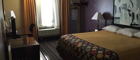 A hotel room with a bed, a desk, a chair, an air conditioner, and a painting on the wall.
