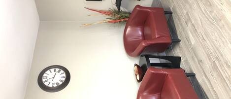 A reception area with two red leather chairs, a wall clock, a black speaker, and a plant.