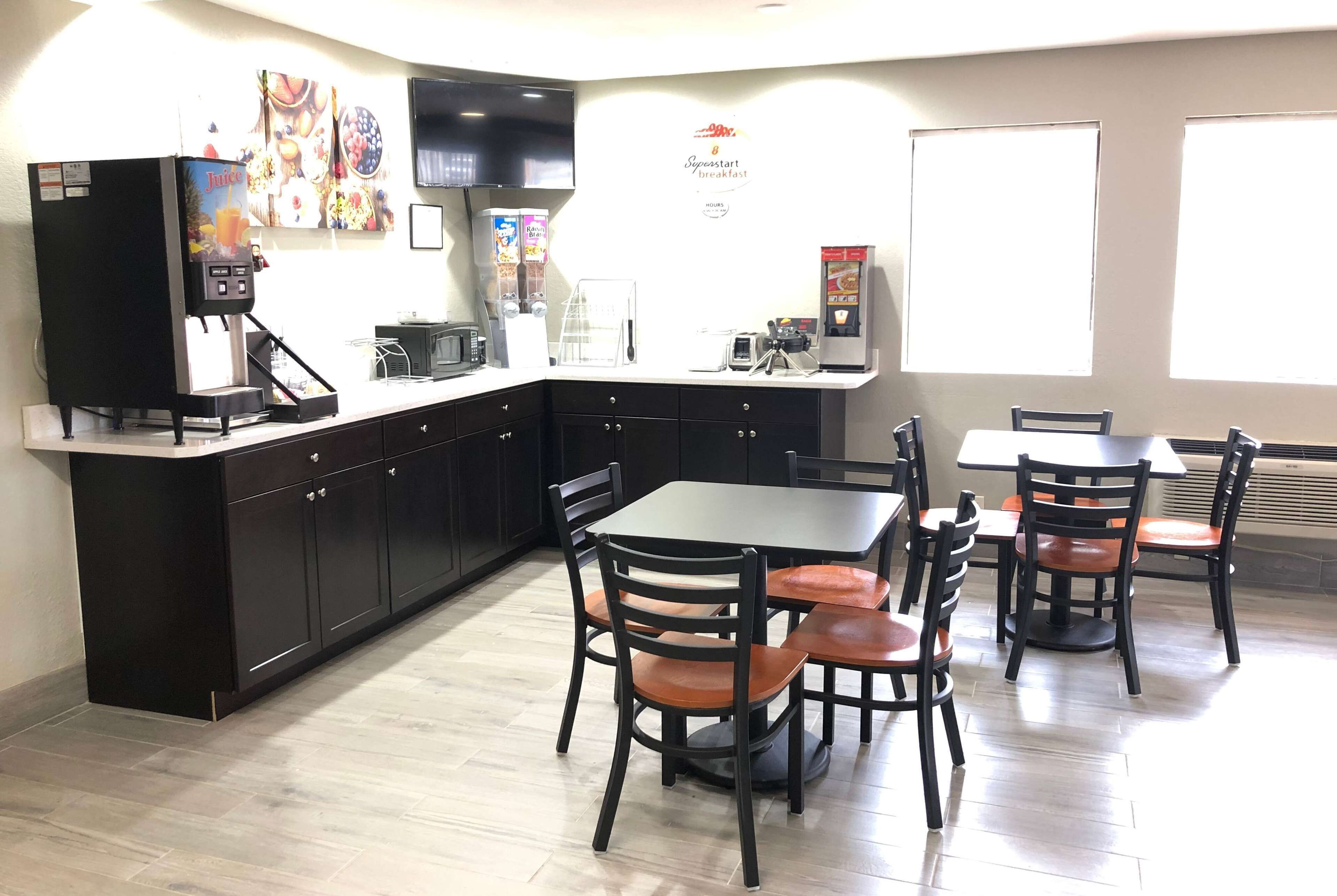 A modern kitchen with a coffee machine, a microwave, and a refrigerator. There is a dining area with a table and chairs.