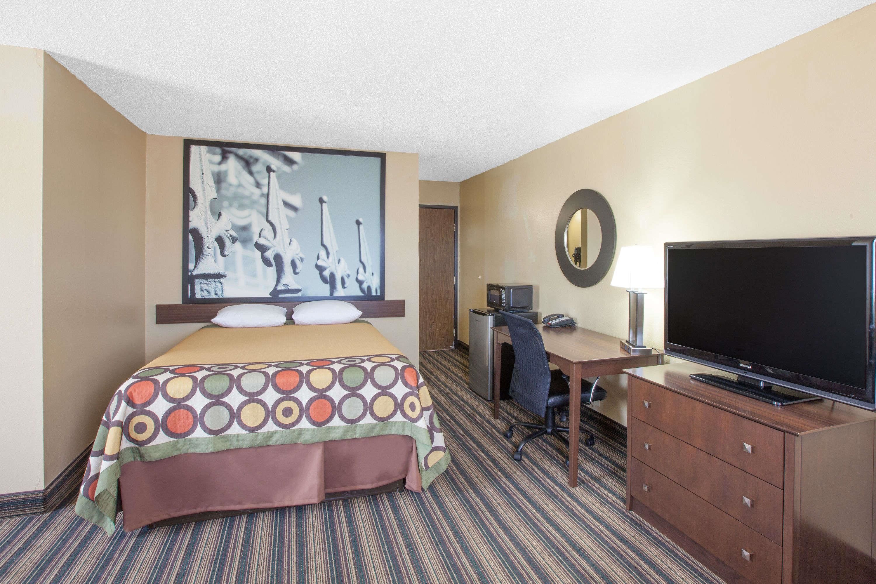 A hotel room with a bed, a desk with a computer, a TV, and a mirror.