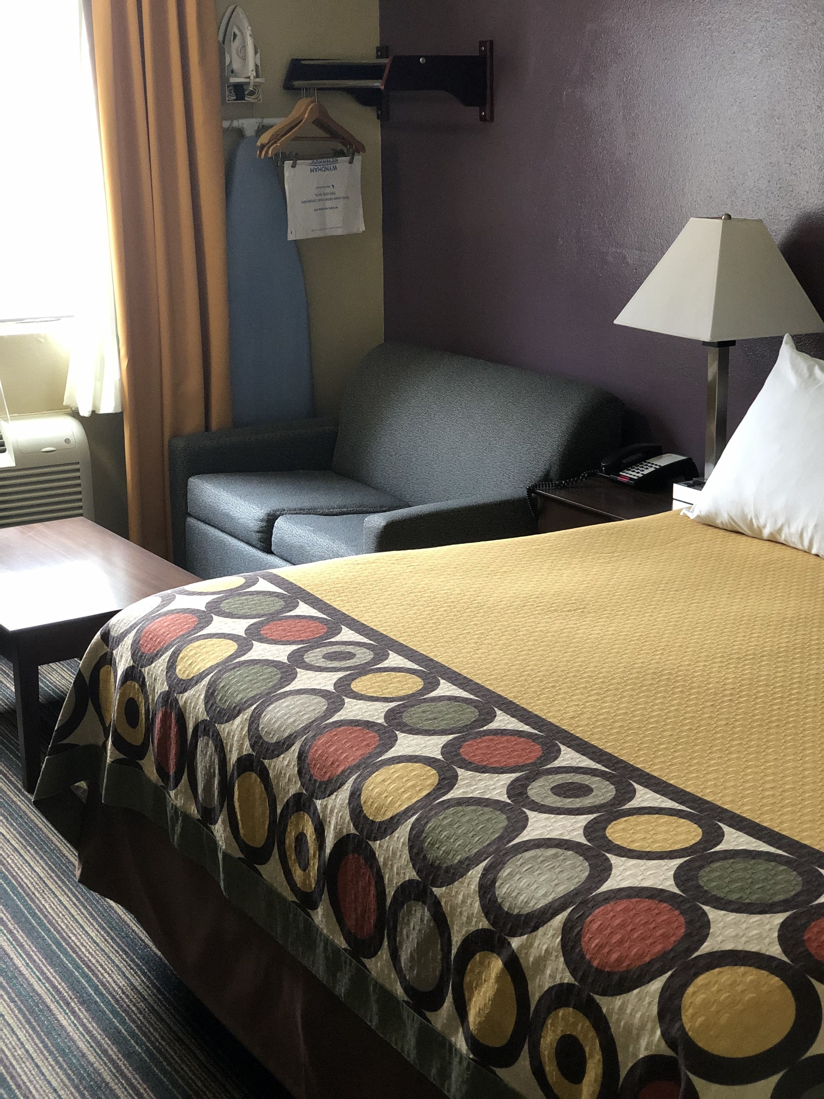 A hotel room with a bed, a desk, a chair, a lamp, and a telephone.