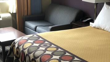 A hotel room with a bed, a desk, a chair, a lamp, and a telephone.