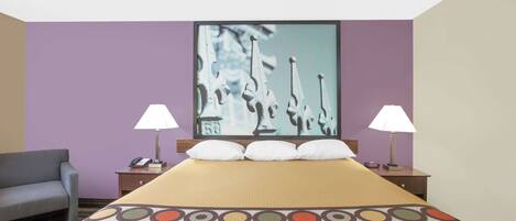 Quarto de hotel com uma cama, duas luminárias de cabeceira, uma mesa de cabeceira com telefone e uma cadeira.