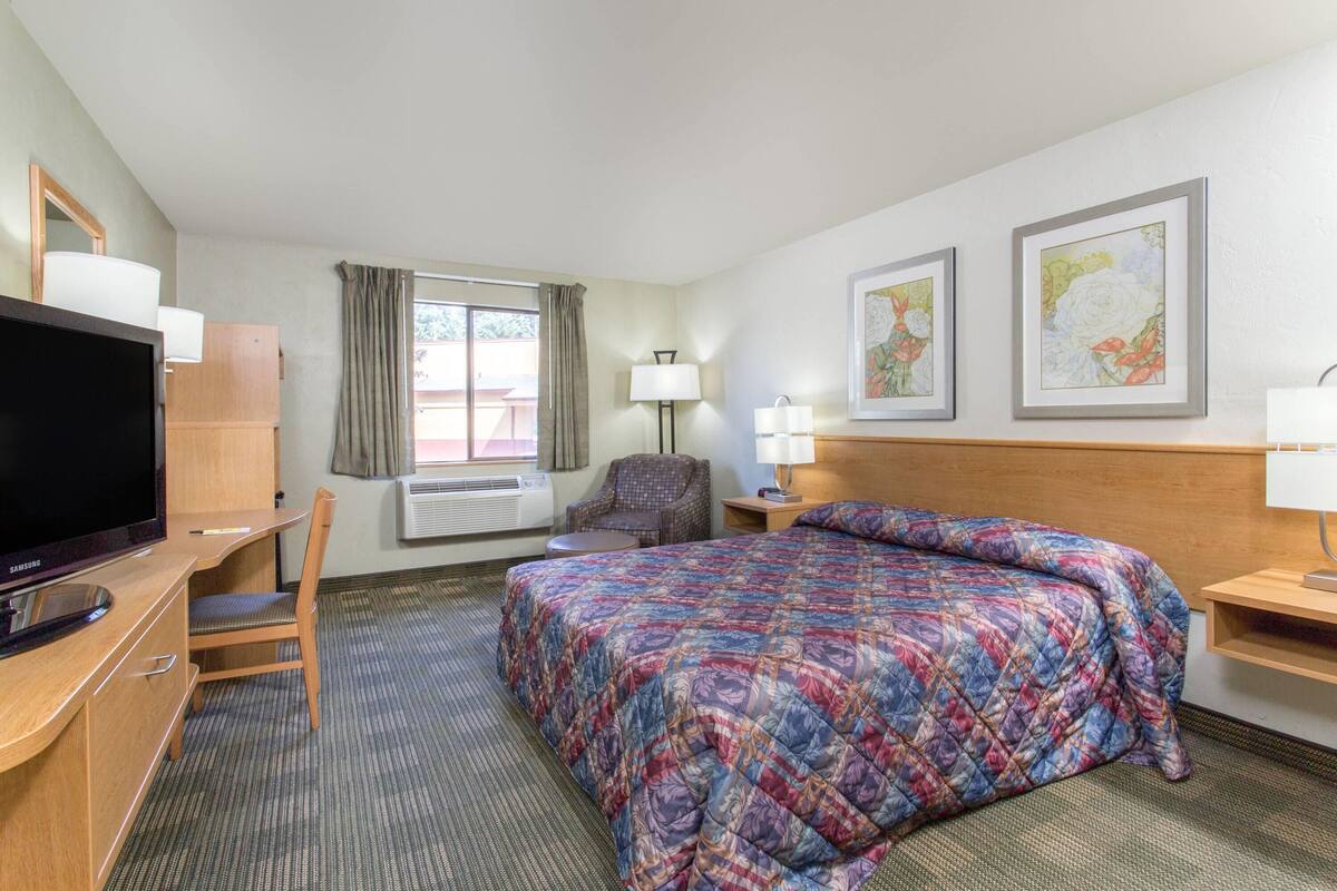 A hotel room with a bed, a desk with a TV, a chair, a lamp, and two framed pictures on the wall.