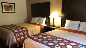 Une chambre d’hôtel avec deux lits, chacun recouvert d’une couvre-lit à motifs, une table de chevet avec une lampe et un tableau encadré au mur.