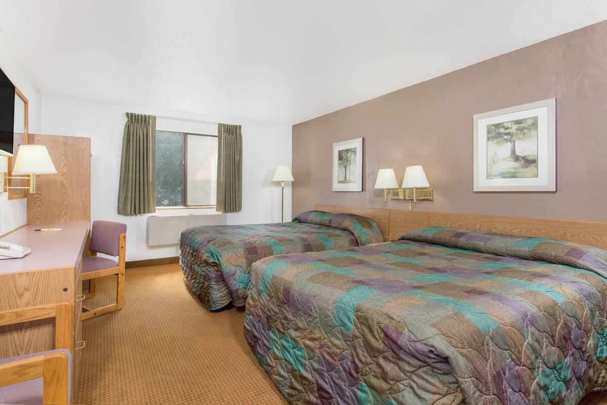 A hotel room with two beds, a desk, a chair, and two lamps.