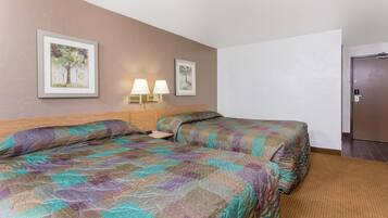 Une chambre d’hôtel avec deux lits, une tête de lit en bois, deux lampes fixées au mur et deux tableaux encadrés accrochés au mur.