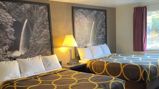 A hotel room with two beds, each with a patterned bedspread, a nightstand with a lamp, and two large framed pictures of waterfalls on the wall. - Super 8 by Wyndham Lacey Olympia Area (Lacey)
