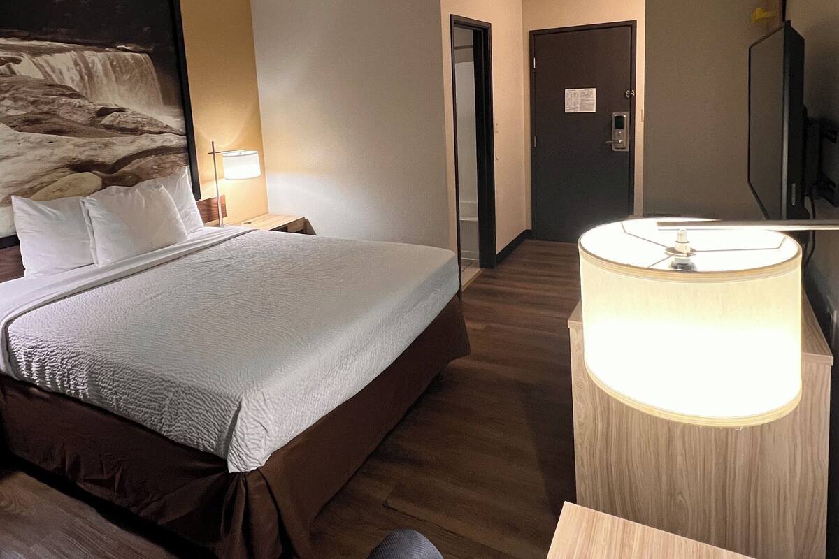 A hotel room with a bed, bedside table, lamp, and a television.