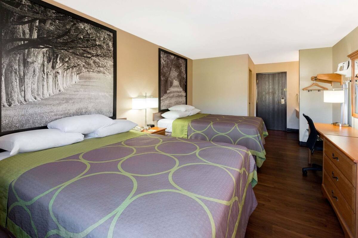 A hotel room with two beds, a desk, a chair, a lamp, and a door.