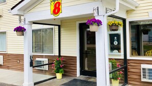 A hotel entrance with a sign reading "Super 8", a covered porch with hanging flower baskets, and a door with a glass panel. - Super 8 by Wyndham Radcliff Ft. Knox Area (Radcliff)