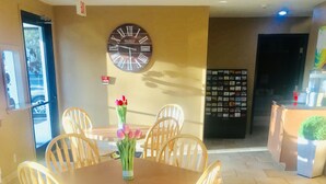 A dining area with a wooden table and chairs, a clock on the wall, and a bouquet of flowers on the table. - Super 8 by Wyndham Radcliff Ft. Knox Area (Radcliff)