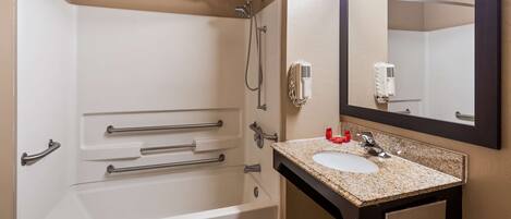 A bathroom with a bathtub, a sink with a granite countertop, and a mirror above the sink.