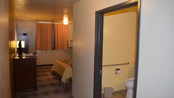 A hotel room with a bed, a desk with a lamp, a bathroom with a toilet and shower.