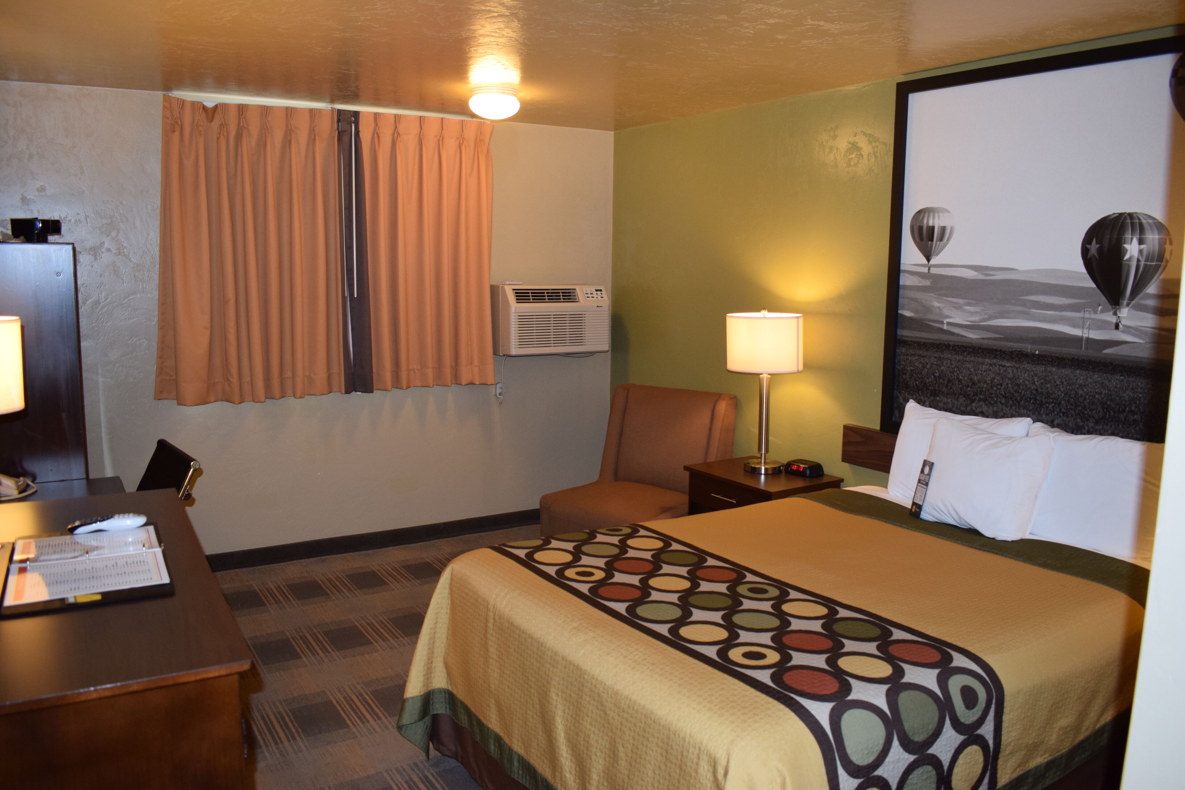 A hotel room with a bed, a desk, a chair, a lamp, and a wall-mounted air conditioner.