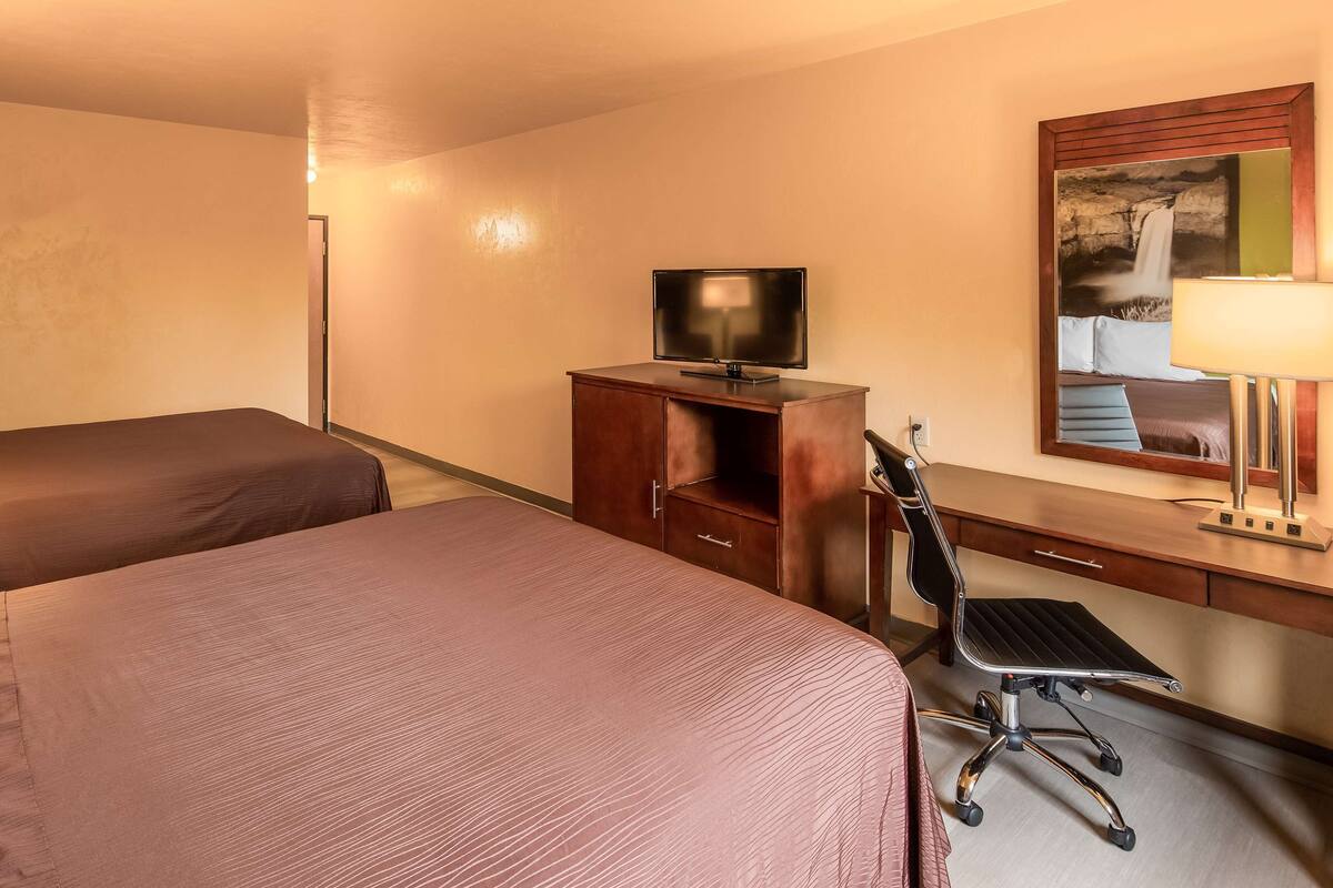 A hotel room with two beds, a desk, a chair, a TV, and a mirror.