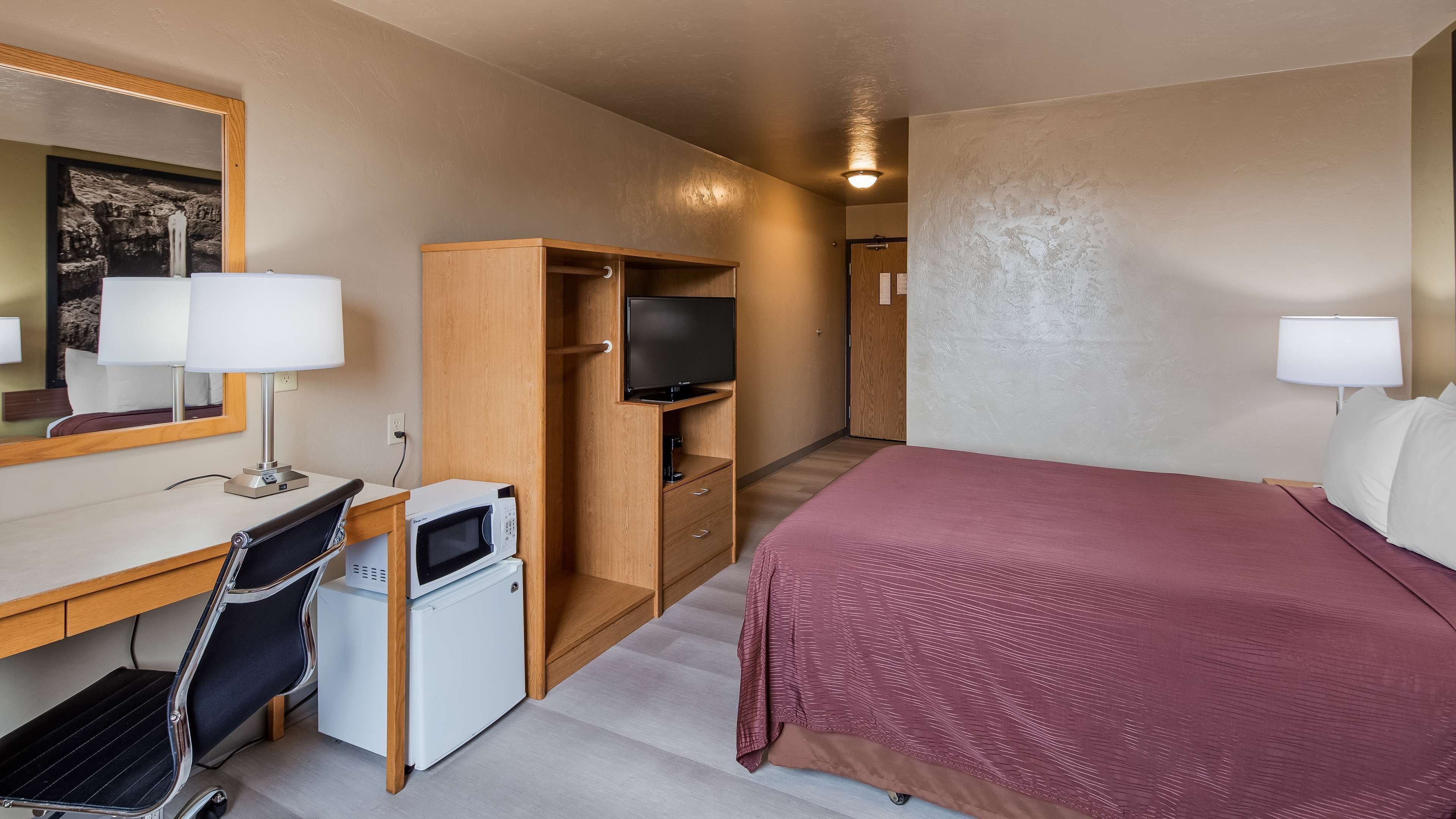 Une chambre d’hôtel comprenant un lit, un bureau avec un ordinateur et un micro-ondes, une télévision, une armoire et un miroir.