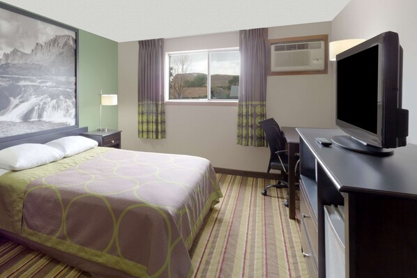 Quarto de hotel com cama, secretária com computador, televisão e janela com cortinas.
