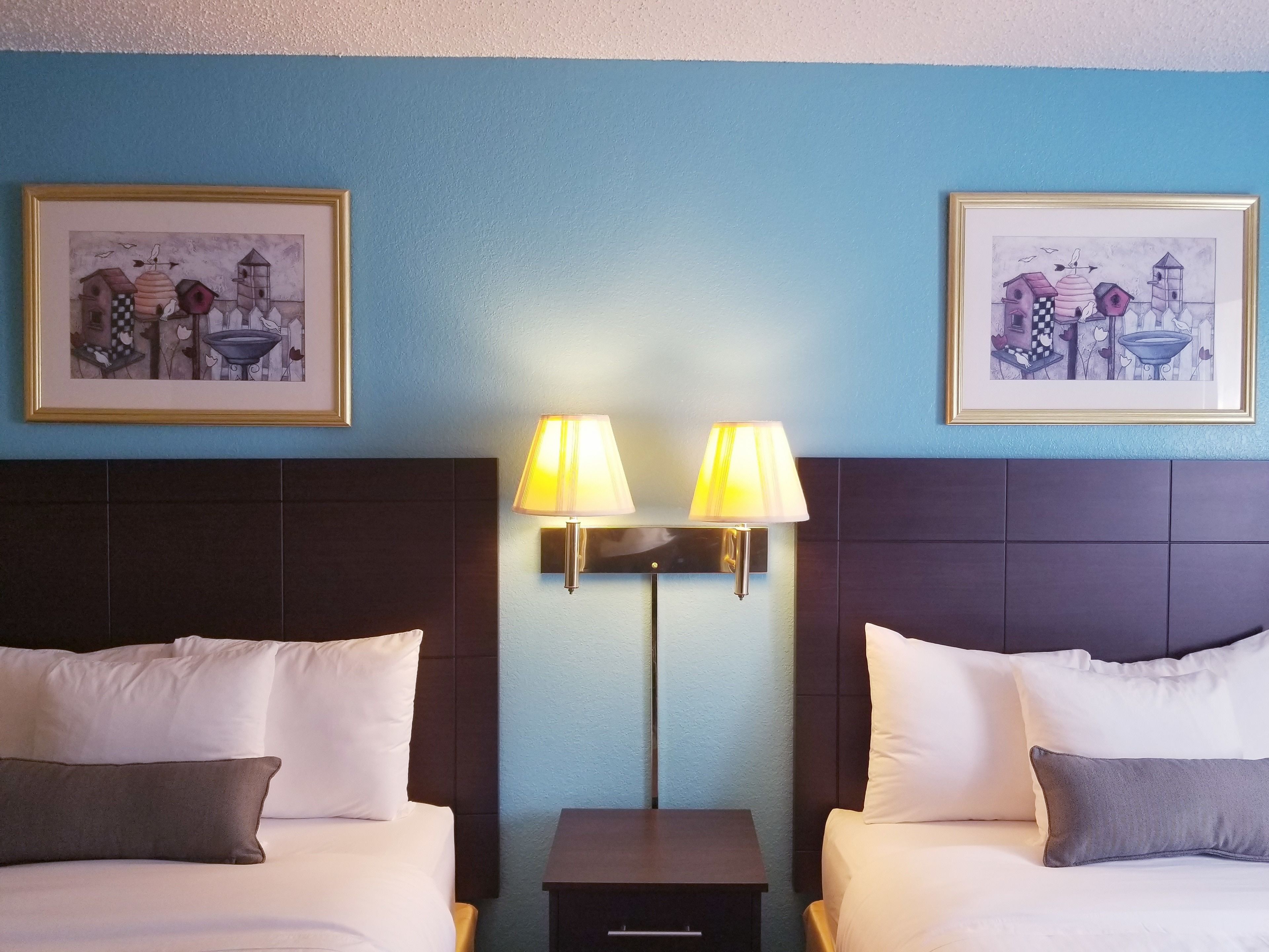 A hotel room with two beds, a nightstand, and two wall-mounted lamps.