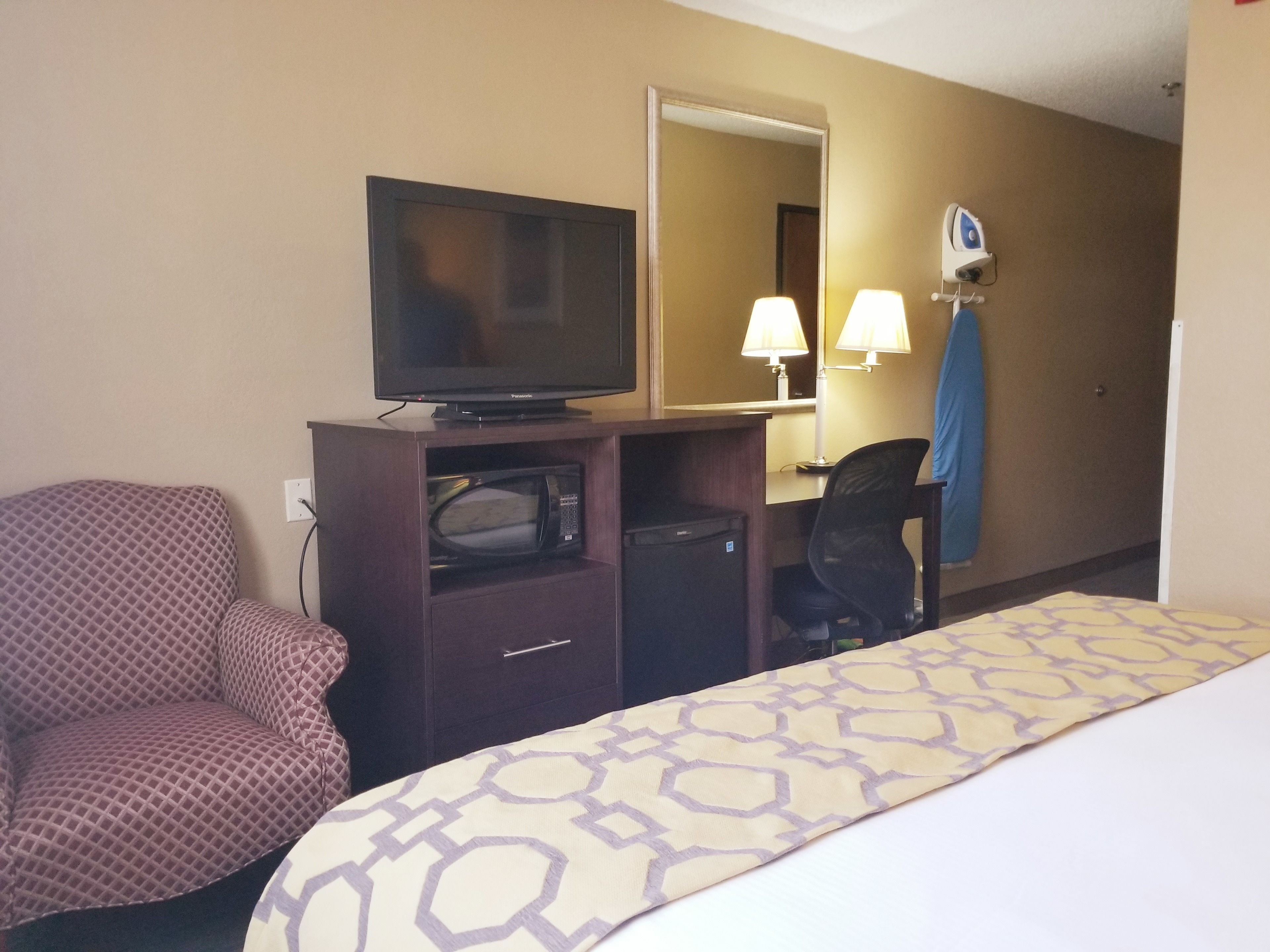 A hotel room with a bed, a television on a wooden cabinet, a microwave, a desk with a lamp, and a chair.