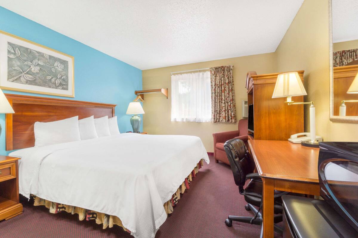 Ein Hotelzimmer mit einem großen Bett, einem Schreibtisch mit Telefon, einem Stuhl und einer Lampe.
