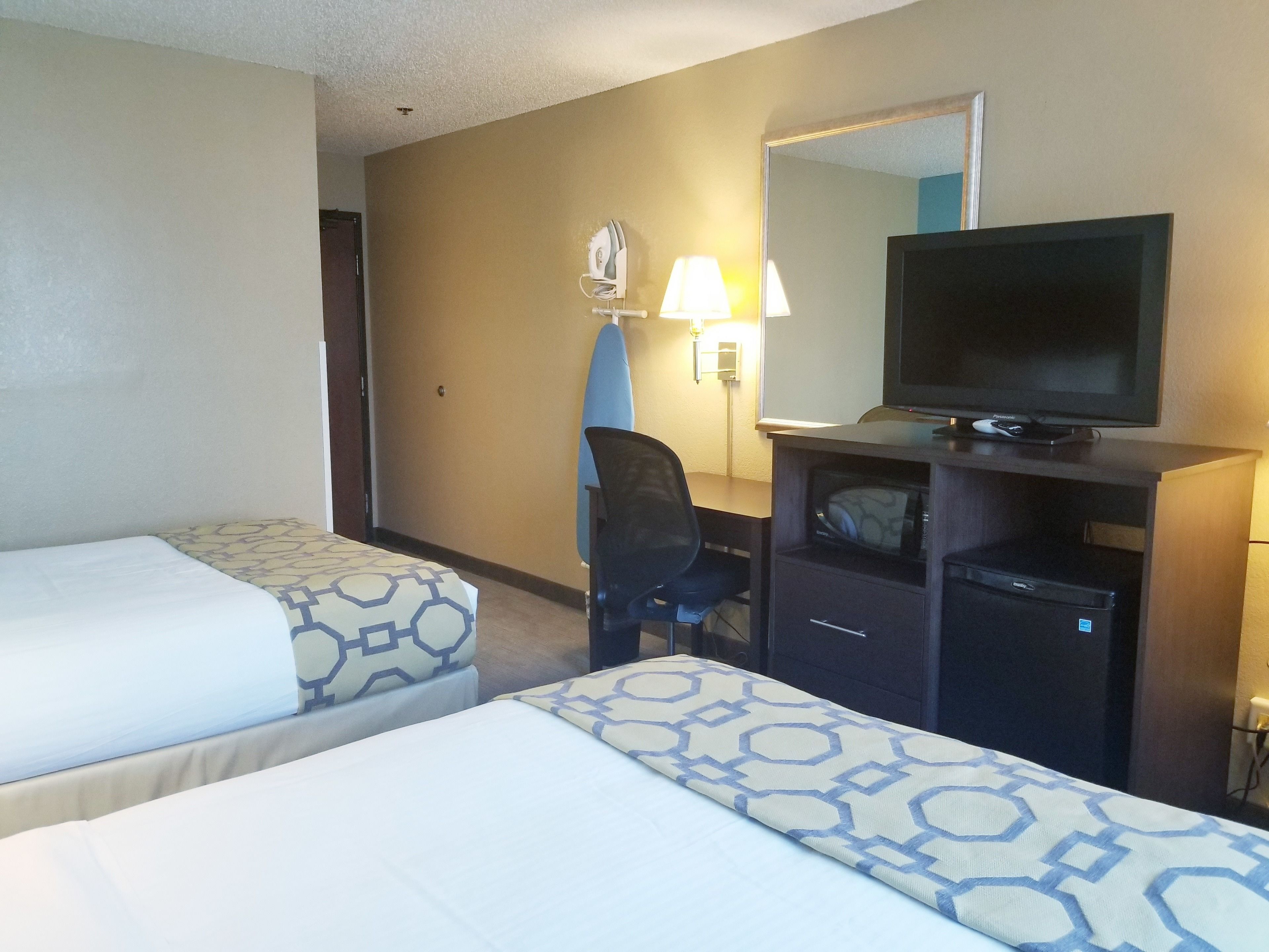 A hotel room with two beds, a desk with a television, a chair, and a mirror.