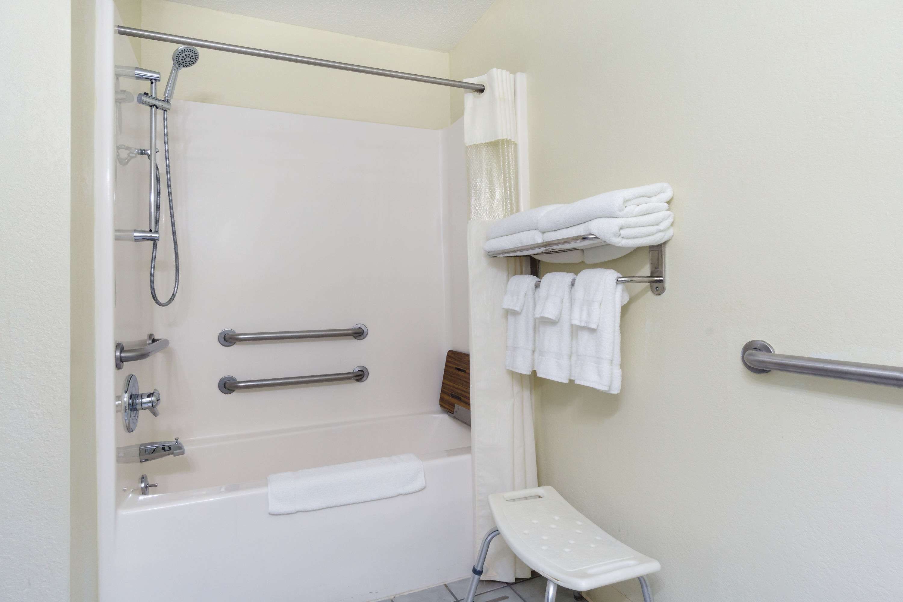 A bathroom with a bathtub, a shower, and a handrail. There are towels hanging on a rack and a step stool.