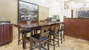 A dining area with a wooden table and chairs, a painting on the wall, and a kitchen area with a microwave and sink. - Super 8 by Wyndham Riverton (Riverton)