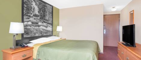 Een hotelkamer met een bed, twee nachtkastjes met lampen, een televisie op een houten dressoir, en een groot gepoft foto van een waterval aan de muur.