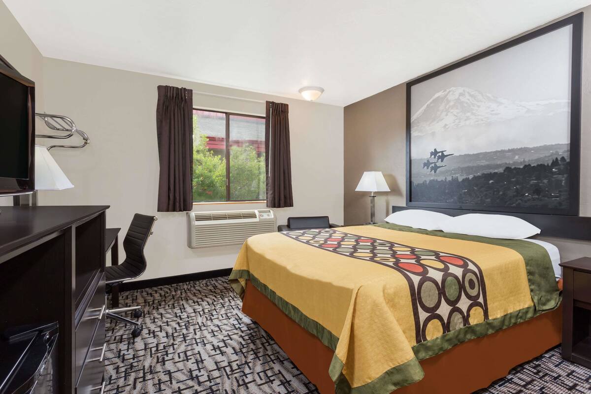 Ein Hotelzimmer mit Bett, Schreibtisch, Stuhl und einem großen Fenster mit Vorhängen.