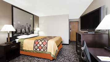 A hotel room with a bed, two bedside lamps, a desk with a chair, a flat-screen TV, and a cityscape artwork on the wall.