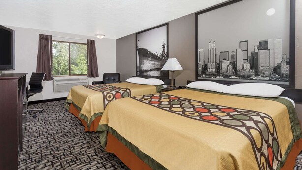 A hotel room with two beds, a desk with a chair, a television, a window with curtains, and a cityscape poster on the wall.